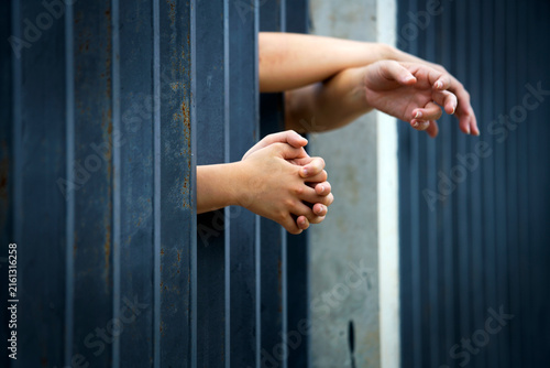 Child’s Hands Clutching Prison Cell Bars with Outstretched Hands Behind Fence