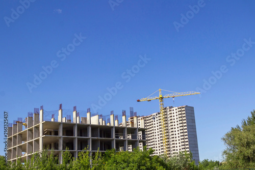 Against the background of a blue sky are unfinished floors of a building, a construction crane and a building under construction