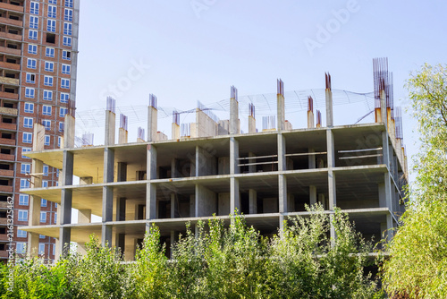 The frame of several unfinished floors of the building. Bushes around.