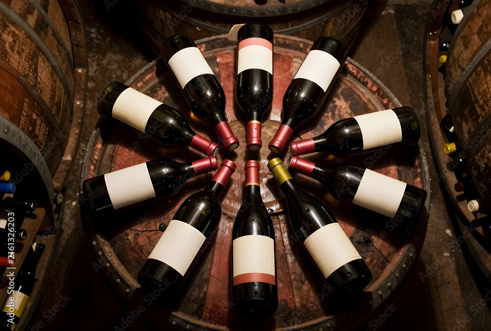 Fototapeta premium Wine tasting and cellar storage, red wine bottles arranged on a wooden barrel in a dark winery
