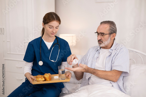 The elderly man was being cared for at home by a private nurse for his illness. The nurse brought him medication to take before bedtime and checked on his condition to monitor his health.