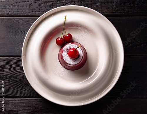 a white plate with a dessert and cherry on a dark wooden table
