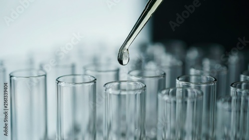 Laboratory pipette dropping clear liquid into a row of empty glass test tubes for scientific analysis with analysis