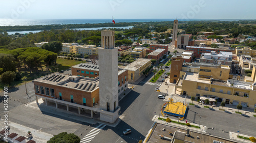 Canvas Print Aerial daytime view of Sabaudia town center in Italy with the rationalist civic tower and central piazza in the foreground, and the coastline, lagoon and open sea visible in the distance