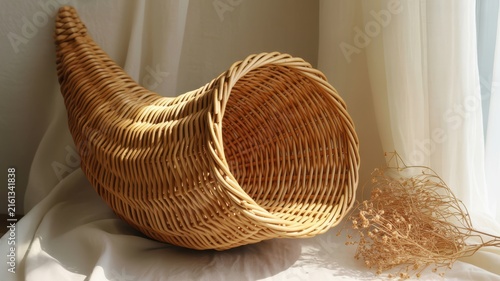 Thanksgiving Empty woven wicker cornucopia horn of plenty resting on a soft white fabric with dried floral accents for decoration USA