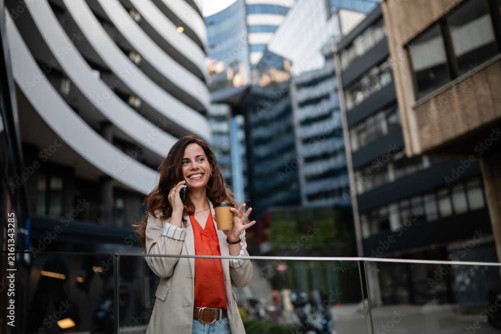 Obraz premium Professional woman talking on smartphone drinking coffee in city