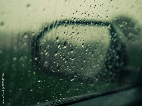 Quadro su tela Raindrops covering a car window with a blurred side mirror view in a rainy autum