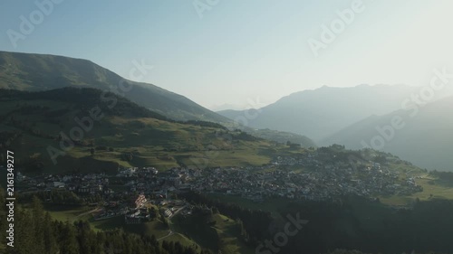 Aerial footage of scenic mountains and green forests under a cloudless blue sky during summer.
