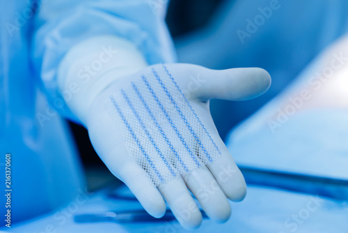 Принти на полотні Surgeon holding medical mesh in gloved hand during procedure after umbilical her