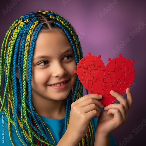 Young girl with colorful braids holds a red heart puzzle