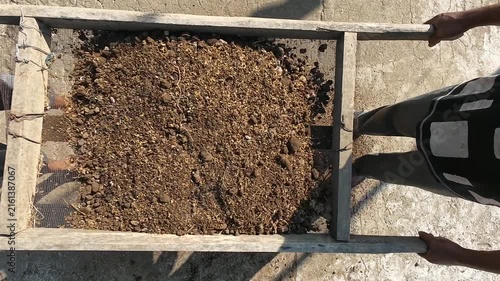 Top view of two farmers sifting organic planting media with handmade wire mesh sieve separating coarse soil and rice husks to produce fine fertile growing medium for sustainable agriculture