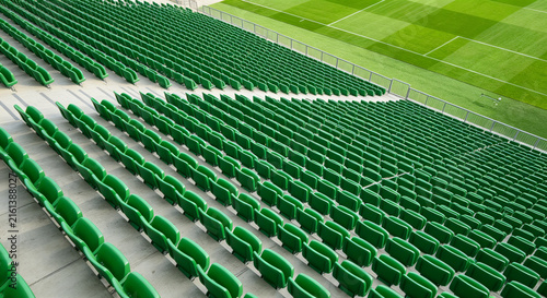 Rows of green plastic seats in empty sports stadium grandstand next to grass pitch