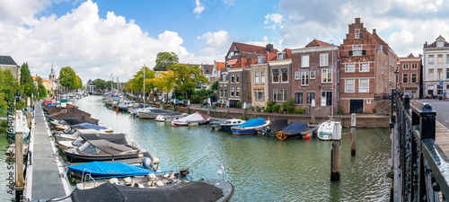 This panoramic image shows the historic Wijnhaven in Dordrecht, surrounded by characteristic townhouses and warehouses, with various pleasure boats moored on the water.