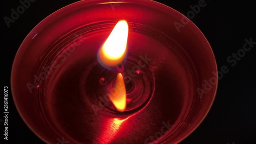Burning tealight candle against dark background, flickering flame creating warm reflections, atmospheric illumination and glowing light for relaxation, meditation, decoration and romantic ambience
