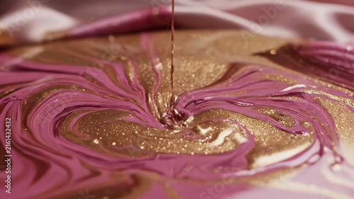 Close-up of swirling pink and purple liquid with shimmering gold accents on a glossy surface