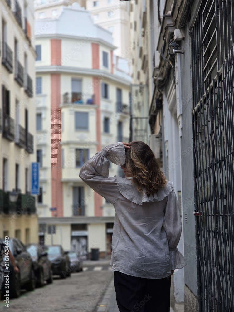 Fototapeta premium Rear view of a woman in a beige ruffled blouse walking along a narrow street in Madrid Spain