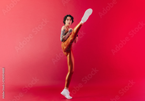 Slim female athlete practicing a leg kick over a crimson background