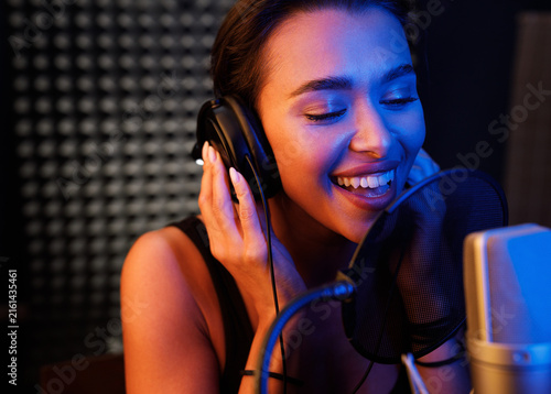 Young smiling female singer performing in a studio under colorful lights