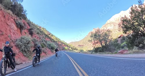 Scenic spring morning e-bike ride through Zion National Park in Utah, USA. Cyclists pedal along dramatic red rock canyons and green trails under soft morning light in this stunning national park lands