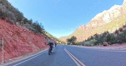 Scenic spring morning e-bike ride through Zion National Park in Utah, USA. Cyclists pedal along dramatic red rock canyons and green trails under soft morning light in this stunning national park lands