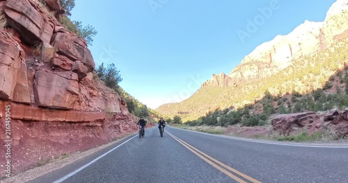 Scenic spring morning e-bike ride through Zion National Park in Utah, USA. Cyclists pedal along dramatic red rock canyons and green trails under soft morning light in this stunning national park lands