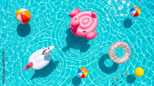 Top down view of colorful inflatable pool floats and beach balls floating in turquoise swimming pool water