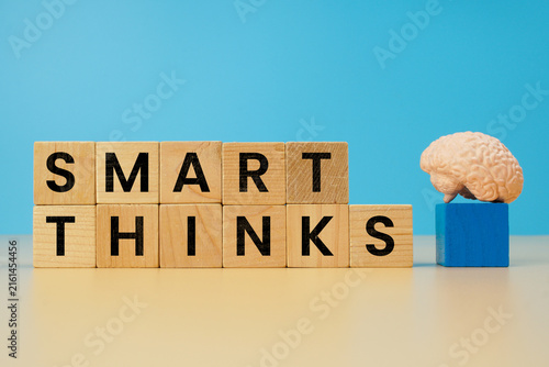 Smart thinks concept with wooden letter blocks and miniature human brain model on blue background, representing intelligence, creative thinking, ideas and problem solving.