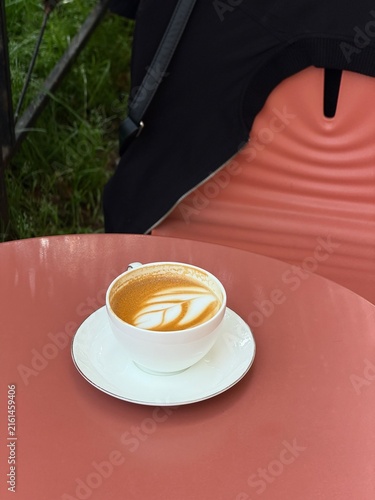 Cappuccino coffee cup on cafe outdoor terrace. Dark red table background, black jacket hanging on a chair, no people. Coffee spot hang out and meeting place theme