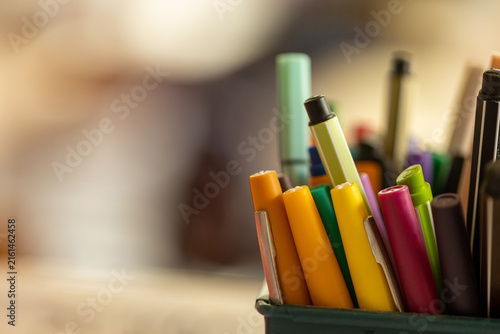 Photography Assortiment de crayons et de fournitures scolaires colorés dans un pot, photographié avec une faible profondeur de champ et une salle de classe floue en arrière-plan