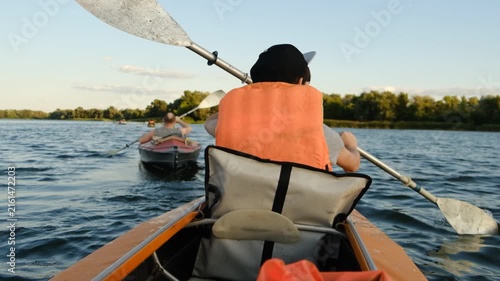 Back view of people kayaking on a calm river during summer sunset.