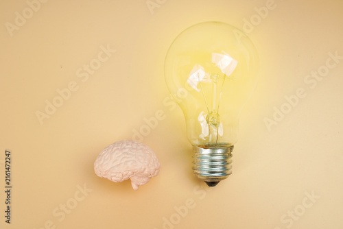 фотографія Human brain model beside a glowing light bulb on yellow background, representing creative ideas, innovation, intelligence, inspiration, thinking and problem solving