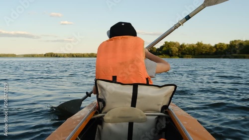 Boy in life jacket kayaking on calm river water during sunny summer day, outdoor active lifestyle and water sport concept