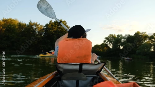 Back view of people kayaking on a calm river during summer sunset.