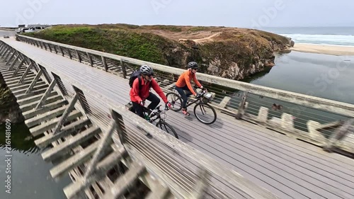A mature man and woman bike together over Pudding Creek bridge on the coastal trail in Fort Bragg near Mendocino, California.