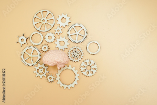 Quadro su tela Human brain model surrounded by wooden gears on yellow background, representing cognitive processes, brain function, thinking, intelligence, problem solving and mental mechanisms