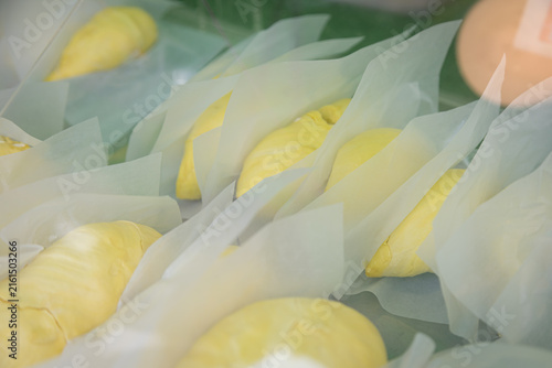 Fresh durian fruits wrapped in white paper, displayed in a market or store setting with a warm light, highlighting the distinctive yellow color and spiky texture of the fruit.