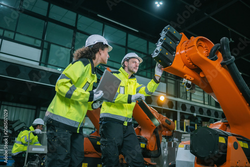 Industrial engineers inspects orange robotic arm automated machinery in warehouse factories. Concept industrial maintenance service, equipment quality inspection, procurement for smart manufacturing.
