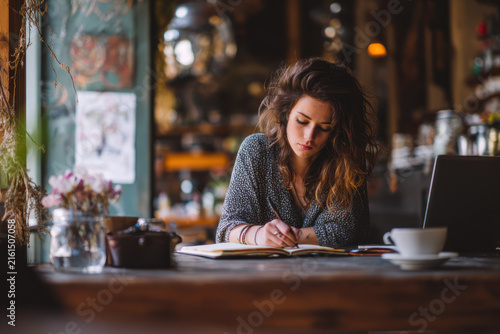 Young woman writing in notebook working in cafe