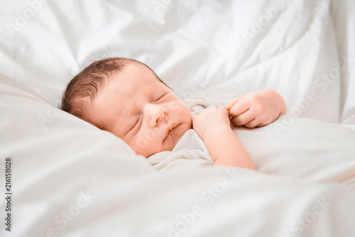 Obraz na plátně Sleeping newborn baby boy wearing a white bodysuit, peacefully resting in a soft white blanket