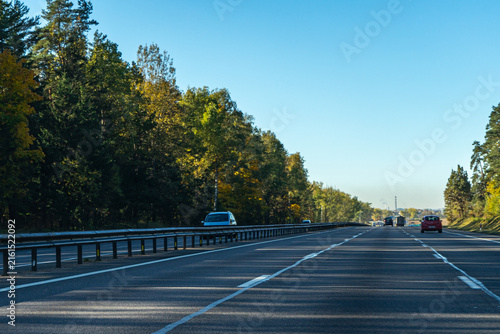 Multi-lane highway road passing along a dense autumn forest with cars on a sunny day