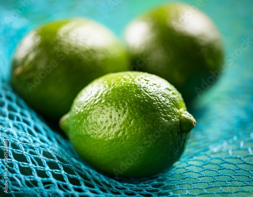macro close up of fresh green limes behind turquoise mesh netting