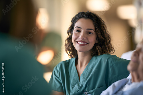 A smiling Hispanic female nurse in green scrubs engages warmly with a patient, showcasing compassion and care in a healthcare setting.
