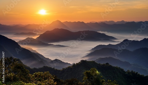 sun rises over a misty valley with layers of mountains