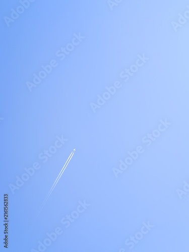 A vertical minimalist shot of a jet airplane flying high in a clear blue sky leaving a white contrail