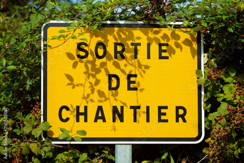 Foto Panneau de signalisation « Sortie de chantier » installé au bord d’une route, entouré de ronces et de végétation en pleine nature