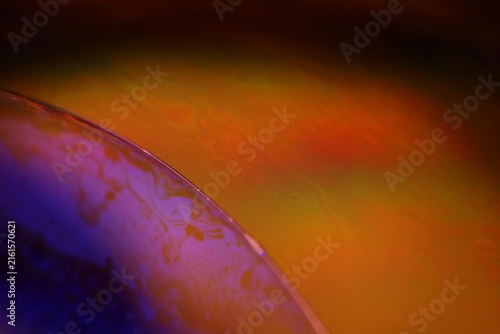 Dual-tone fluid film horizon with purple dome and glowing amber plane. A sharp specular rim arc separates two distinct fluid zones in low-key macro perspective.