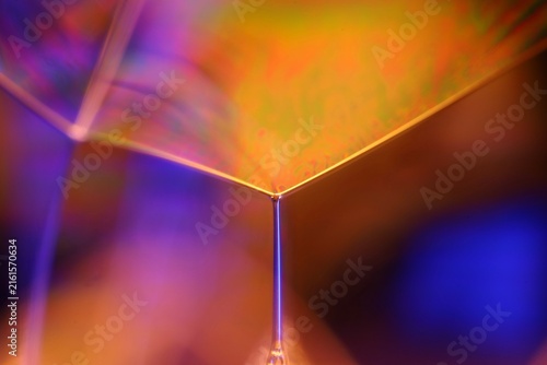 Geometric liquid film vertex with warm amber plane and purple background bokeh. Sharp specular rim lines converge into a central liquid film vertex in low-key macro perspective