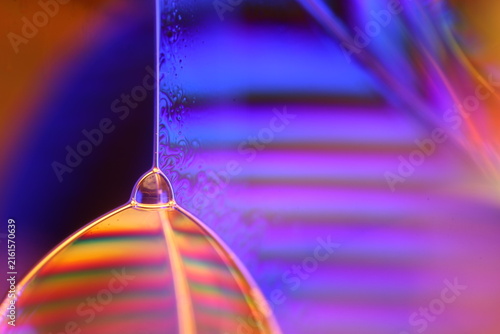 Vibrant liquid film vertex with colorful interference bands and blue bokeh. A sharp vertical specular line meets a glowing fluid film vertex in low-key macro perspective