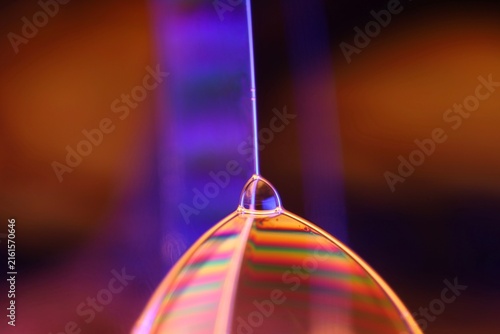 Glowing liquid film vertex with rainbow interference dome and purple backlighting. A sharp vertical specular rim line meets an illuminated liquid film vertex in low-key macro perspective.