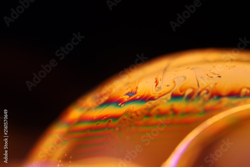 Iridescent golden liquid film dome with rainbow interference bands. Warm golden and amber backlighting illuminates a curved fluid dome horizon.